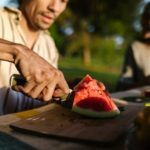 man slicing watermelon on brown wooden chopping board