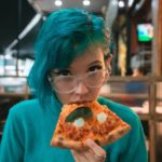 green haired woman eating pizza